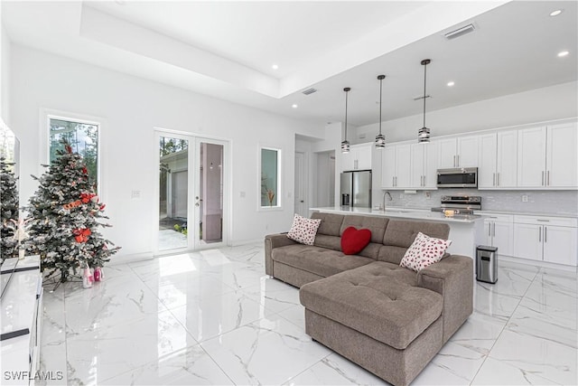 living room featuring french doors, a raised ceiling, and sink