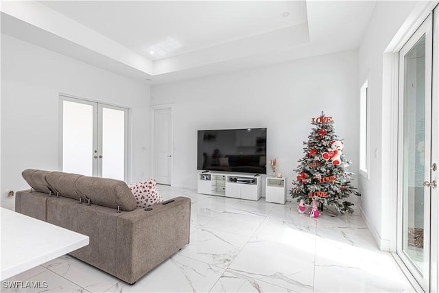 living room featuring a raised ceiling, a healthy amount of sunlight, and french doors