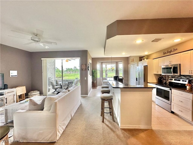 kitchen with a breakfast bar, a kitchen island, ceiling fan, stainless steel appliances, and white cabinets