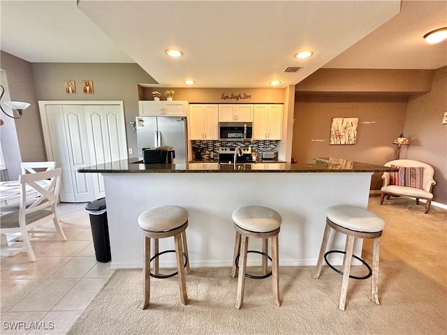 kitchen with white cabinetry, a breakfast bar area, dark stone countertops, and appliances with stainless steel finishes