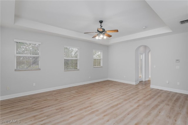 unfurnished room featuring a tray ceiling, ceiling fan, and light wood-type flooring