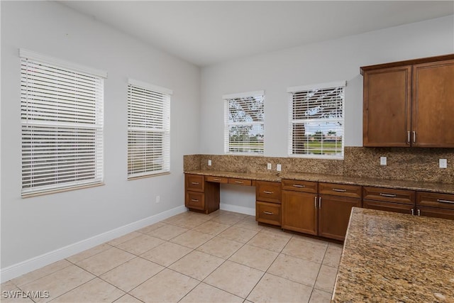 kitchen with dark stone countertops, light tile patterned floors, built in desk, and decorative backsplash