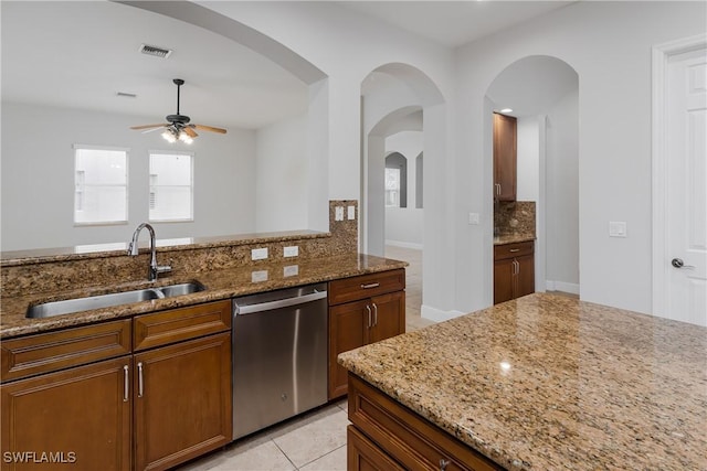 kitchen featuring light stone counters, stainless steel dishwasher, sink, and decorative backsplash