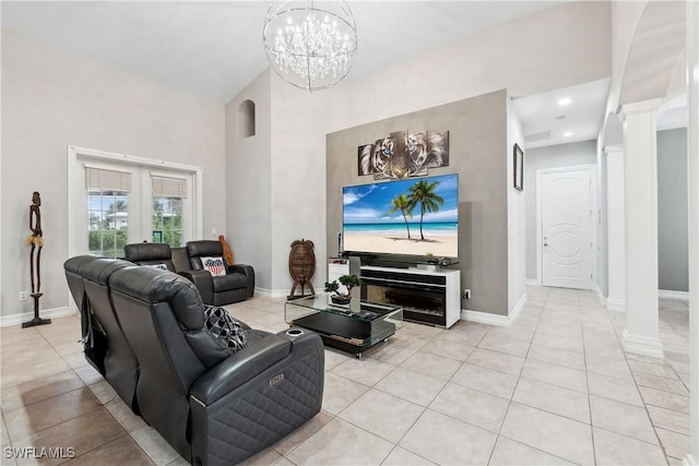 living room with light tile patterned floors, a towering ceiling, a chandelier, and ornate columns