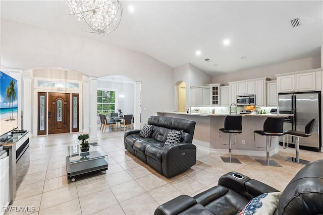 living room featuring lofted ceiling, sink, decorative columns, a notable chandelier, and light tile patterned flooring