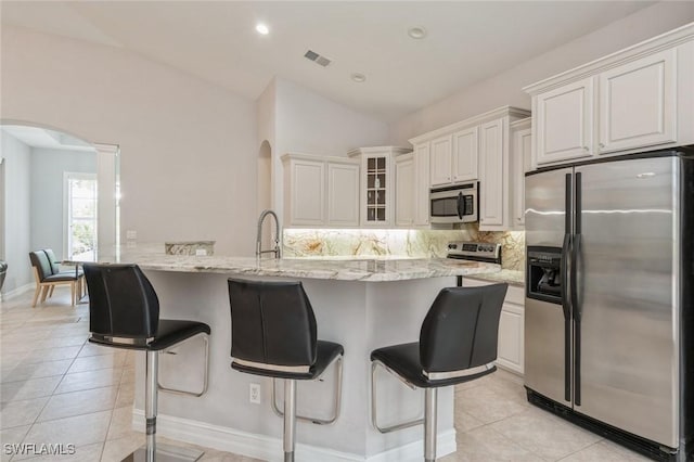 850 25th St SW, Naples, FL 34117 - kitchen featuring appliances with stainless steel finishes, arched walkways, light tile patterned floors, tasteful backsplash, and a breakfast bar