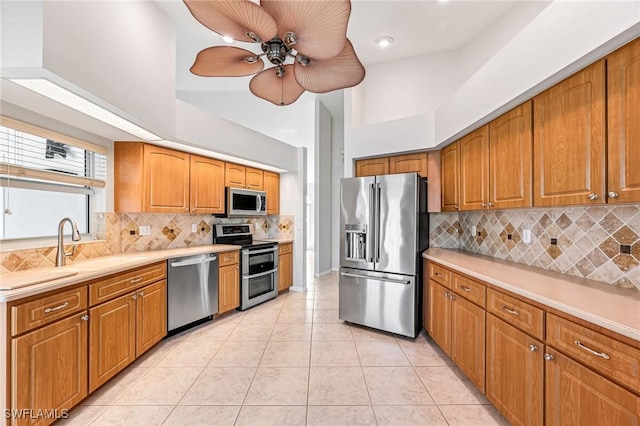 kitchen featuring sink, tasteful backsplash, light tile patterned floors, a towering ceiling, and stainless steel appliances