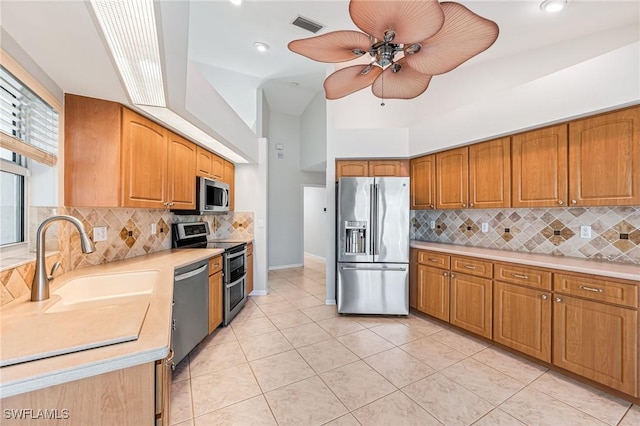 kitchen with sink, light tile patterned floors, ceiling fan, appliances with stainless steel finishes, and backsplash