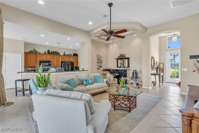 living room featuring a towering ceiling, a fireplace, ceiling fan, and light tile patterned flooring