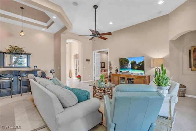 living room featuring crown molding, light tile patterned floors, a tray ceiling, ceiling fan, and a high ceiling