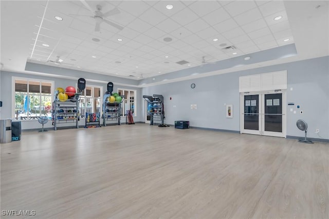 workout area with a raised ceiling, ceiling fan, a drop ceiling, and light hardwood / wood-style floors