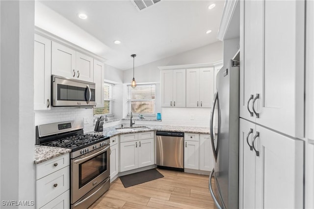 kitchen featuring white cabinetry, light stone counters, decorative light fixtures, vaulted ceiling, and stainless steel appliances