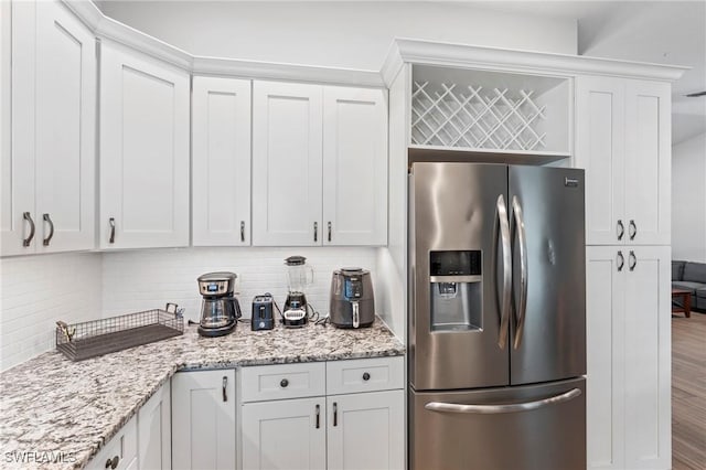 kitchen with hardwood / wood-style floors, white cabinets, decorative backsplash, light stone counters, and stainless steel refrigerator with ice dispenser