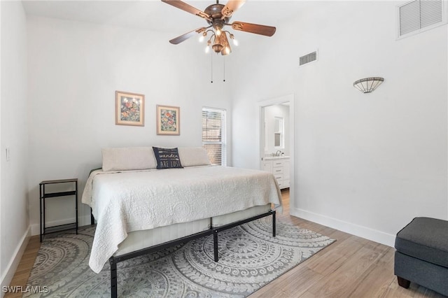 bedroom featuring a towering ceiling, light hardwood / wood-style flooring, ceiling fan, and ensuite bathroom