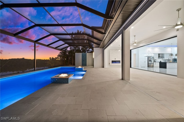 pool at dusk with a patio, a lanai, an outdoor kitchen, and ceiling fan