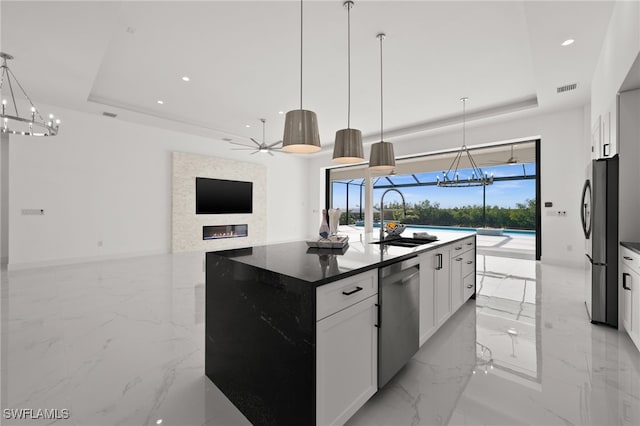 kitchen with white cabinetry, stainless steel appliances, a tray ceiling, and a center island with sink