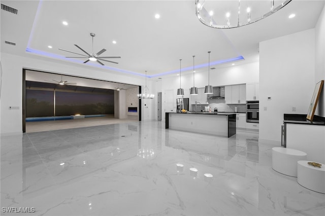 kitchen featuring wall chimney range hood, white cabinetry, a kitchen island, decorative light fixtures, and a raised ceiling