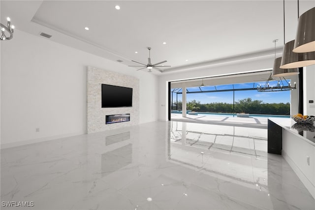 unfurnished living room featuring a raised ceiling and ceiling fan with notable chandelier