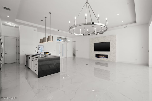 kitchen with pendant lighting, sink, white cabinetry, a center island with sink, and a raised ceiling