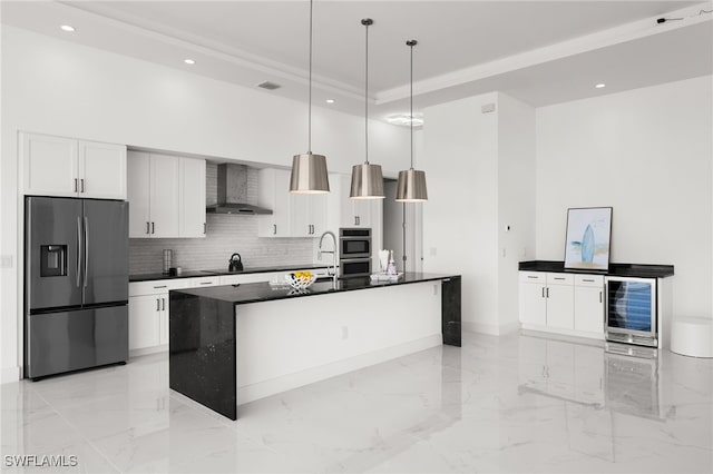 kitchen with white cabinetry, appliances with stainless steel finishes, pendant lighting, a kitchen island with sink, and wall chimney range hood