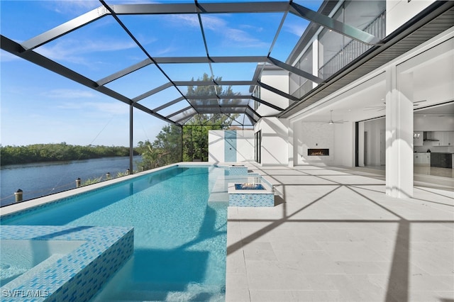 view of swimming pool with a patio area, a water view, glass enclosure, an outdoor fire pit, and ceiling fan