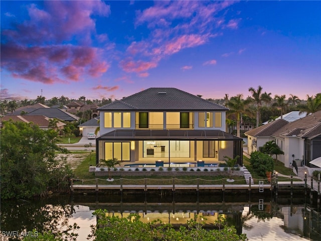 back house at dusk with a water view and a yard