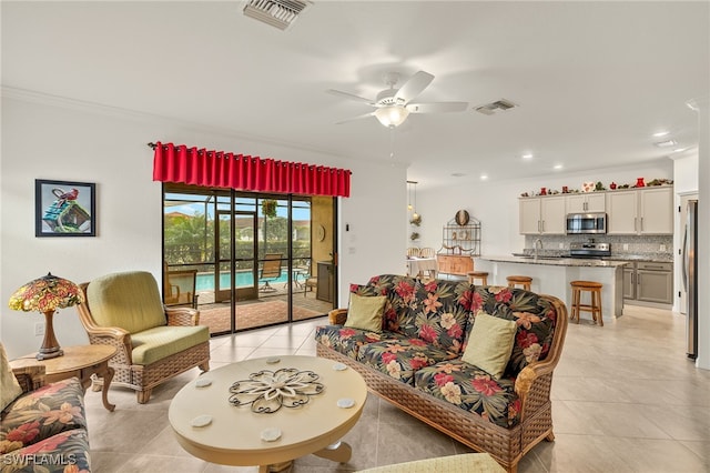 living room featuring crown molding, sink, light tile patterned floors, and ceiling fan