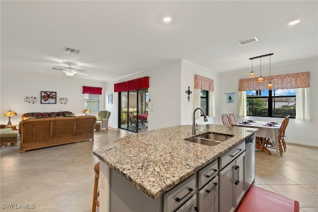 kitchen with pendant lighting, sink, a kitchen island with sink, crown molding, and light stone countertops