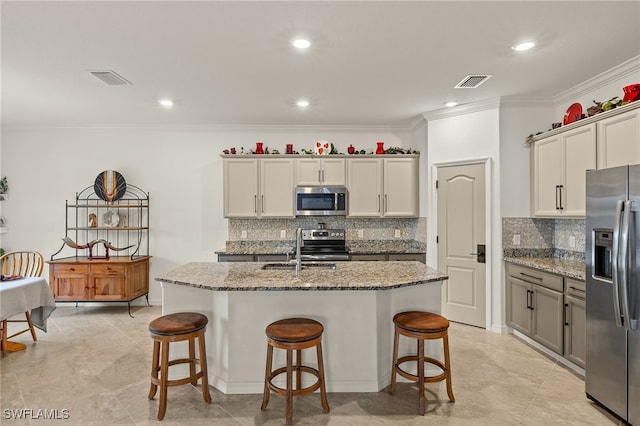 kitchen with light stone countertops, appliances with stainless steel finishes, a center island with sink, and crown molding