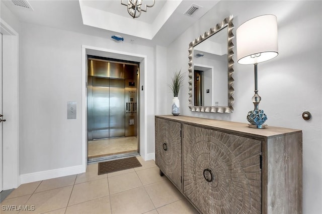 bathroom with tile patterned flooring, elevator, and a tray ceiling