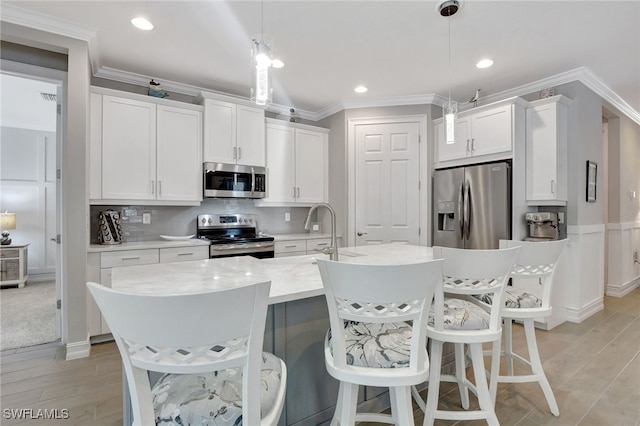 kitchen featuring a breakfast bar, white cabinetry, hanging light fixtures, appliances with stainless steel finishes, and an island with sink