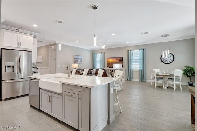 kitchen featuring pendant lighting, sink, appliances with stainless steel finishes, white cabinetry, and an island with sink