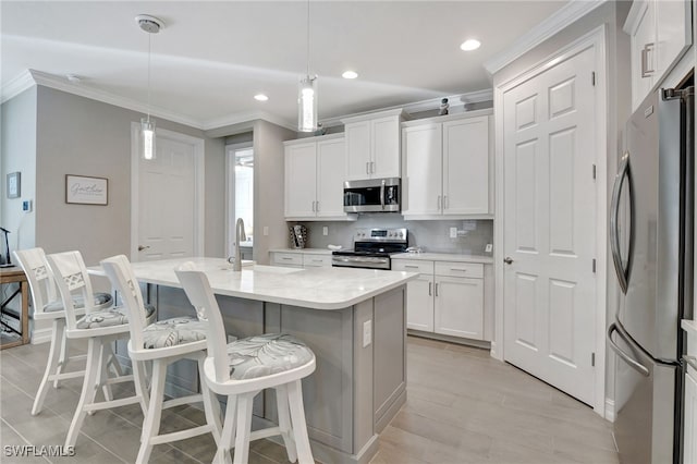 kitchen with pendant lighting, stainless steel appliances, an island with sink, and white cabinets