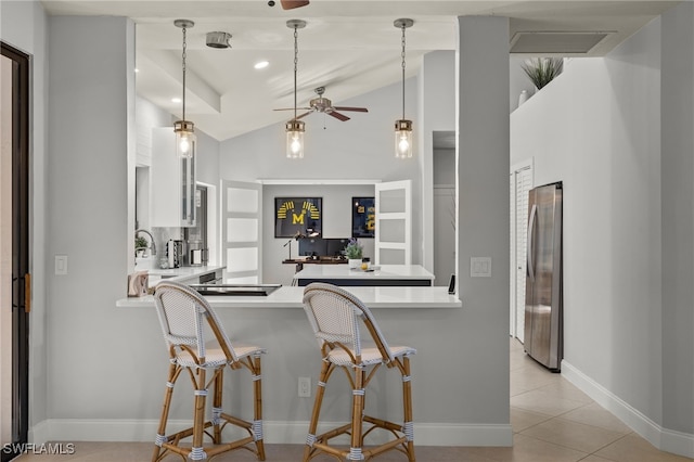 kitchen with a breakfast bar area, decorative light fixtures, vaulted ceiling, stainless steel fridge, and kitchen peninsula