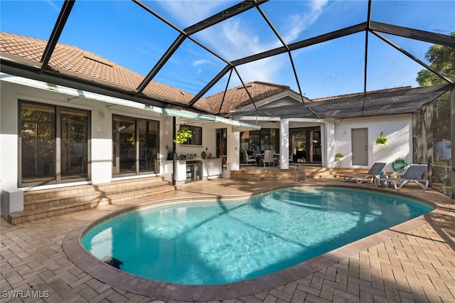 view of pool with a lanai, an outdoor kitchen, and a patio area