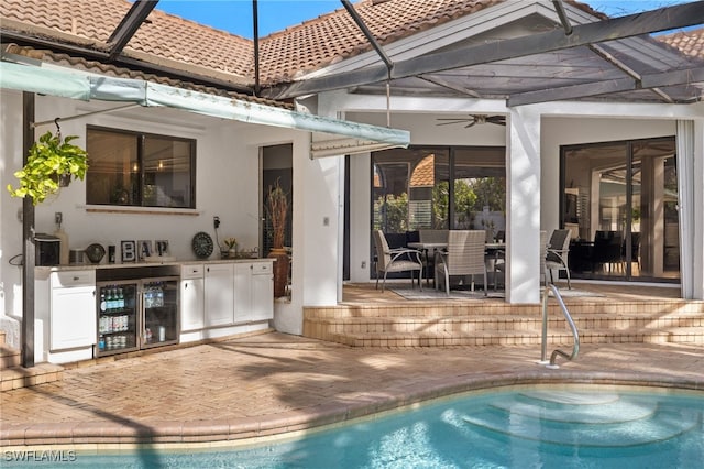 rear view of property featuring a patio, wine cooler, exterior kitchen, ceiling fan, and glass enclosure