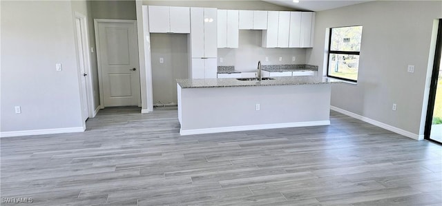 kitchen with a sink, white cabinetry, baseboards, light wood-type flooring, and an island with sink