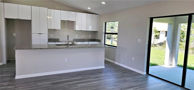 kitchen with a sink, white cabinets, vaulted ceiling, dark wood-style floors, and a center island with sink