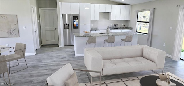 kitchen featuring a kitchen island with sink, a sink, light wood-style floors, white cabinets, and stainless steel fridge with ice dispenser