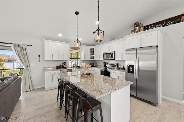 kitchen featuring white cabinetry, stainless steel appliances, light stone counters, a kitchen island, and decorative light fixtures