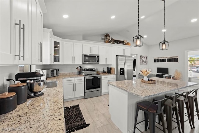 kitchen with pendant lighting, a breakfast bar area, appliances with stainless steel finishes, light stone countertops, and white cabinets