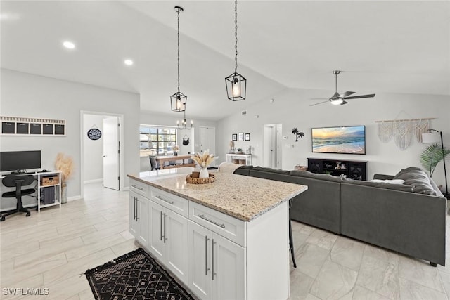 kitchen featuring lofted ceiling, light stone counters, a center island, pendant lighting, and white cabinets