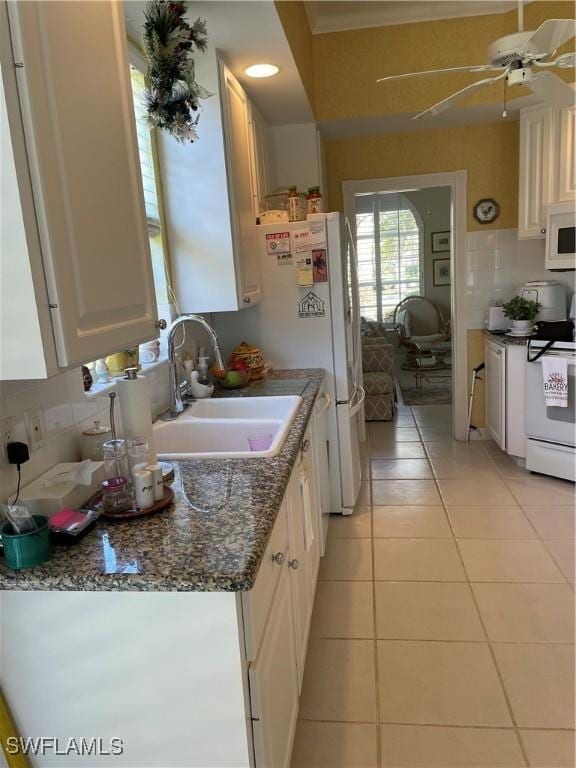 kitchen with sink, white appliances, light tile patterned floors, white cabinetry, and dark stone counters