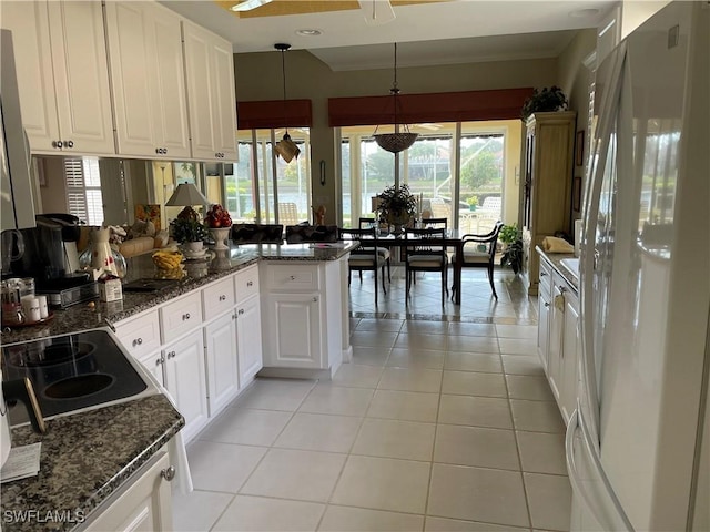 kitchen featuring decorative light fixtures, dark stone countertops, white refrigerator, light tile patterned floors, and white cabinets