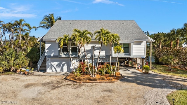 view of front facade featuring a shingled roof, a garage, stairway, and dirt driveway