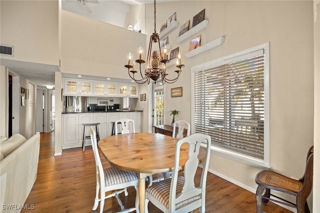 dining space with a chandelier, dark wood-style flooring, visible vents, and a towering ceiling