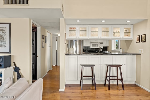 kitchen featuring dark countertops, visible vents, white microwave, stainless steel fridge, and a kitchen bar