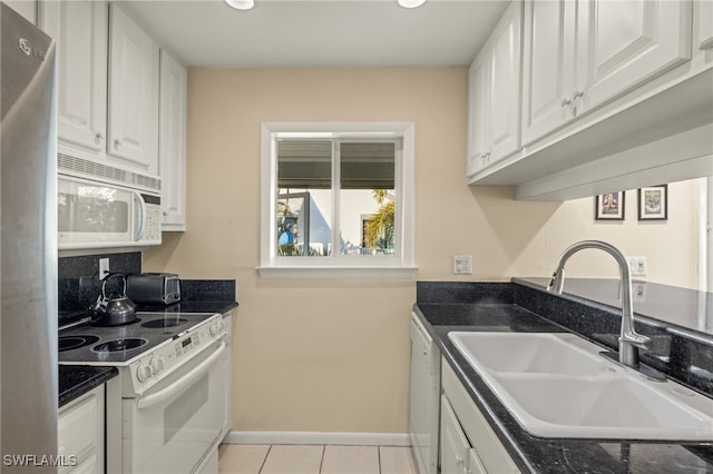 kitchen with white appliances, white cabinets, dark countertops, a sink, and light tile patterned flooring