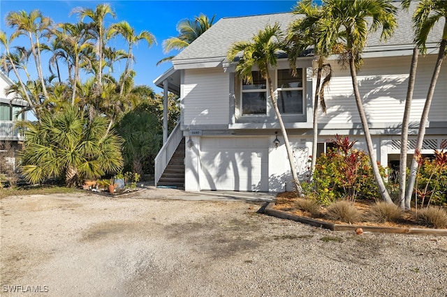 exterior space featuring driveway, a shingled roof, a garage, and stairway