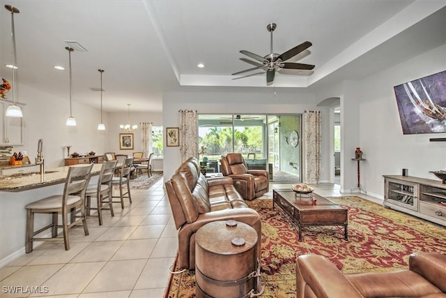 living room with light tile patterned flooring, a tray ceiling, ceiling fan with notable chandelier, and sink